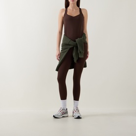 Model wearing brown bodycon mini dress with built-in top, styled with olive green tied shirt, dark leggings, white socks and grey trainers