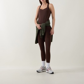 Model wearing dark brown strappy cami top and matching leggings, styled with an olive shirt tied at the waist and grey trainers.