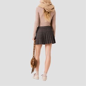 Model carrying a brown fringed bag, styled with a grey pleated mini skirt, beige top, camel scarf and white trainers, shot from behind.