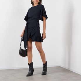 Model wearing Isabel Marant Etoile Melicia Ruffle Mini Dress in black, styled with black cowboy boots and a black shoulder bag.