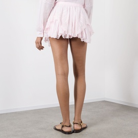 Model wearing Isabel Marant Etoile light pink cotton shorts with ruffled hem, styled with gold-hardware tan sandals, rear view