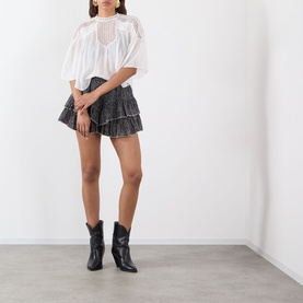 Model wearing Isabel Marant Etoile Jocadia Layered Printed Mini Skirt in black/ecru, tiered ruffle voile, styled with white top and black ankle boots.