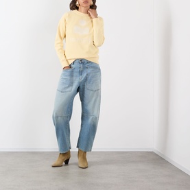 Model wearing Isabel Marant Etoile Millyny Logo Sweatshirt in light yellow, styled with light blue barrel-leg jeans and tan ankle boots.
