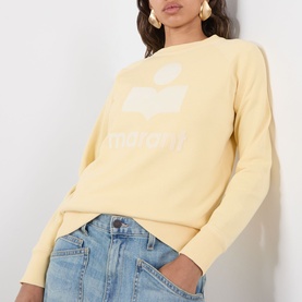 Model wearing Isabel Marant Etoile Millyny Logo Sweatshirt in light yellow, crew neck with ecru logo print, styled with light wash denim jeans.