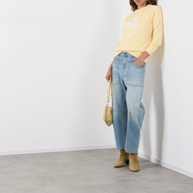 Model wearing Isabel Marant Etoile Millyny Logo Sweatshirt in light yellow, styled with light blue patchwork jeans and tan ankle boots, carrying