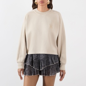 Model wearing beige crew-neck sweatshirt with small chest logo, styled with black floral ruffled mini skirt