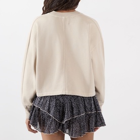 Model wearing cream cropped sweatshirt, rear view, styled with black floral ruffle mini skirt