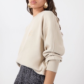 Model wearing a cream oversized sweatshirt with subtle chest detail, styled with a dark floral skirt and gold hoop earrings