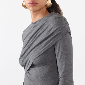 Model wearing Isabel Marant Etoile grey long-sleeve top with draped crossover front detail, gold hoop earrings visible.