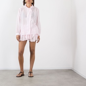 Model wearing Isabel Marant Etoile Leota Ruffle Blouse in light pink with front pleats and ruffled neckline, styled with white shorts and tan sandals.