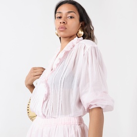 Model wearing Isabel Marant Etoile Leota Ruffle Blouse in light pink with asymmetric ruffled neckline and front pleats, styled with gold earrings and
