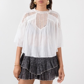 Model wearing white lace-panel cotton blouse with half sleeves, styled with a black floral tiered mini skirt and gold earrings