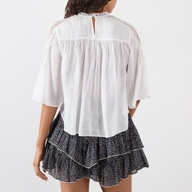 Model wearing white short-sleeve blouse with lace yoke detail, styled with black floral mini skirt, seen from back.