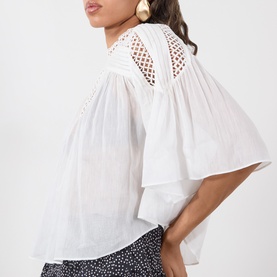 Model wearing white broderie anglaise back detail blouse with flutter sleeves, styled with a black floral print skirt and gold earrings.