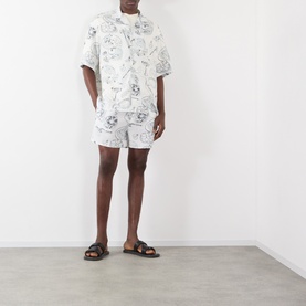 Model wearing Jacquemus Fish Graphic Bowling Shirt in off-white print, styled with matching shorts and black leather slides.