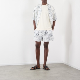 Model wearing Jacquemus Fish Graphic Bowling Shirt in off-white print, styled with matching shorts and black leather sandals.