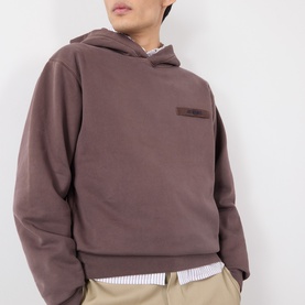 Model wearing Jacquemus brown cotton hoodie, styled with a striped shirt and beige trousers
