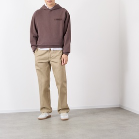 Model wearing Jacquemus brown cotton hoodie with chest logo detail, styled with beige trousers and white trainers.