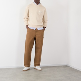 Model wearing Jacquemus beige cotton hoodie with tan trousers, light blue shirt, and white trainers.