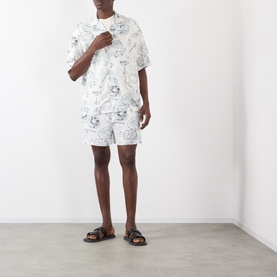 Model wearing Jacquemus Fish Graphic Shorts in off-white with black print, styled with matching graphic tee and dark sandals.