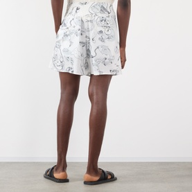 Model wearing Jacquemus Fish Graphic Shorts in off-white with black graphic print, styled with black flat sandals. Rear view.