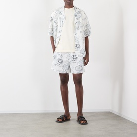 Model wearing Jacquemus Fish Graphic Shorts in off-white print, styled with matching shirt and black sandals.