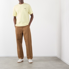Model wearing Jacquemus The Gros Grain Logo T-Shirt in pale yellow with brown chinos and white trainers.