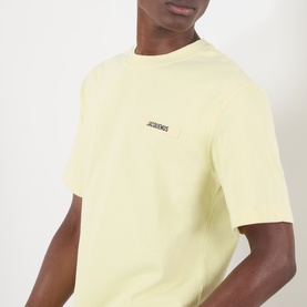 Model wearing Jacquemus The Gros Grain Logo T-Shirt in pale yellow with chest logo patch, round neck and short sleeves.