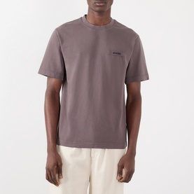 Model wearing Jacquemus brown cotton T-shirt with small chest logo print, styled with cream trousers.