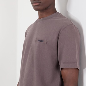 Model wearing Jacquemus brown cotton T-shirt, close-up showing small logo patch on chest pocket area