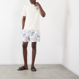 Model wearing Jacquemus The Palmier Logo T-Shirt in Calisson with palm tree graphic, paired with white printed shorts and brown sandals.