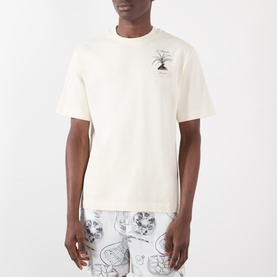 Model wearing Jacquemus The Palmier Logo T-Shirt in Calisson, cream cotton with small palm tree graphic print at chest, styled with printed shorts.