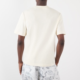 Model wearing Jacquemus The Palmier Logo T-Shirt in Calisson, rear view, short sleeves, straight hem, styled with printed trousers.