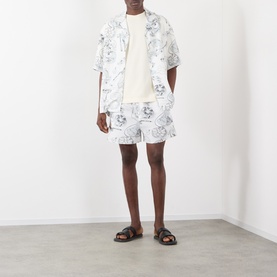 Model wearing Jacquemus The Palmier Logo T-Shirt in Calisson with matching palm print shorts and dark brown sandals.