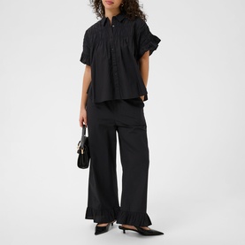 Model wearing Kaffe black deep wide-leg trousers with ruffle hem, styled with matching black short-sleeve blouse and kitten heel mules