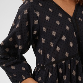Model wearing Kaffe dress in Black Gray Vintage Baroque, featuring V-neckline, long sleeves, and gold geometric print detail.