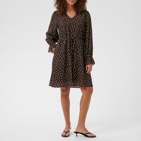 Model wearing black polka dot long-sleeve mini dress with V-neck and elasticated waist, styled with black flat sandals