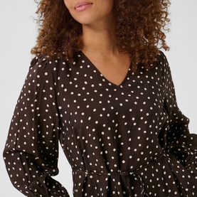 Model wearing dark brown polka dot V-neck blouse with long sleeves and belted waist detail, close-up crop shot