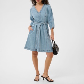 Model wearing light blue denim V-neck belted mini dress with 3/4 sleeves, styled with black heeled sandals and small black handbag
