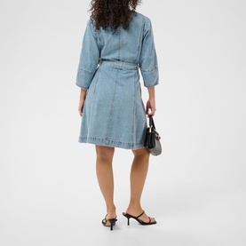 Model wearing light blue denim wrap dress with three-quarter sleeves and belted waist, styled with black strappy heels and small black handbag