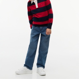 Model wearing Tommy Hilfiger kids' vintage medium stretch jeans in mid-blue wash, styled with a red and navy striped rugby shirt and white trainers.