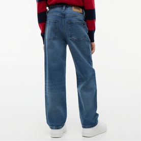 Model wearing Tommy Hilfiger children's vintage medium stretch jeans, rear view, paired with a red and navy striped jumper and white trainers.