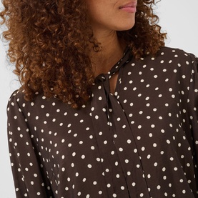 Model wearing Kaffe dress in Coffee Bean with white polka dot print, featuring a tie-neck collar detail, long sleeves visible.