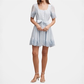 Model wearing pale blue mini dress with lace trim, puff sleeves, square neckline, and tie waist, styled with strappy heels