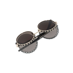 Round sunglasses with gold-tone studded frames, dark grey lenses, and crystal embellishment detail along the rims