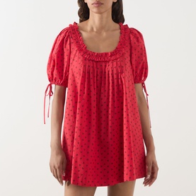 Model wearing Damson Madder Jemima Cherry Mini Dress in Red Cherries, with ruffle scoop neck, puffed short sleeves and self-tie cuffs