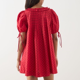 Model wearing Damson Madder Jemima Cherry Mini Dress in red cherries, shown from back, featuring pleated detail and self-tie cuffs.
