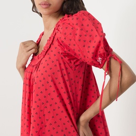 Model wearing Damson Madder Jemima Cherry Mini Dress in red cherries print, showing ruffle neckline and self-tie cuff detail