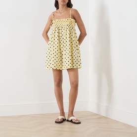 Model wearing Damson Madder Butter Spot cotton mini dress with smocked bodice, spaghetti straps and full skirt, styled with white sandals.