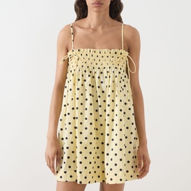 Model wearing Damson Madder Butter Spot mini dress with polka dot print, shirred bust, tie straps, and relaxed silhouette in yellow cotton.
